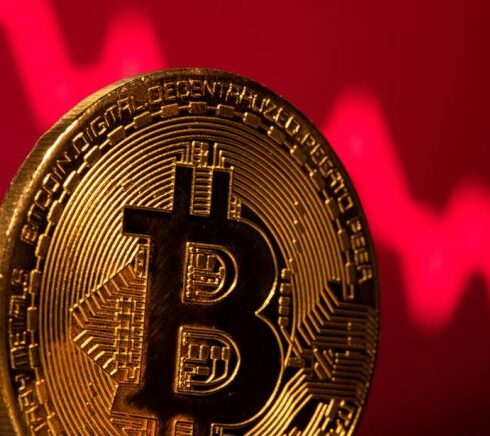 Một biểu trưng của Bitcoin được đặt trước hình minh họa thị trường giảm giá. Ảnh: Reuters