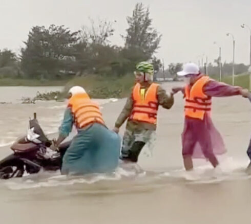 Một người dân đi qua đoạn đường thôn Đông Bình, xã Duy Vinh, huyện Duy Xuyên bị nước cuốn xe máy được nhiều người hợp sức kéo lên chiều 14/12. Ảnh: Nguyễn Nở